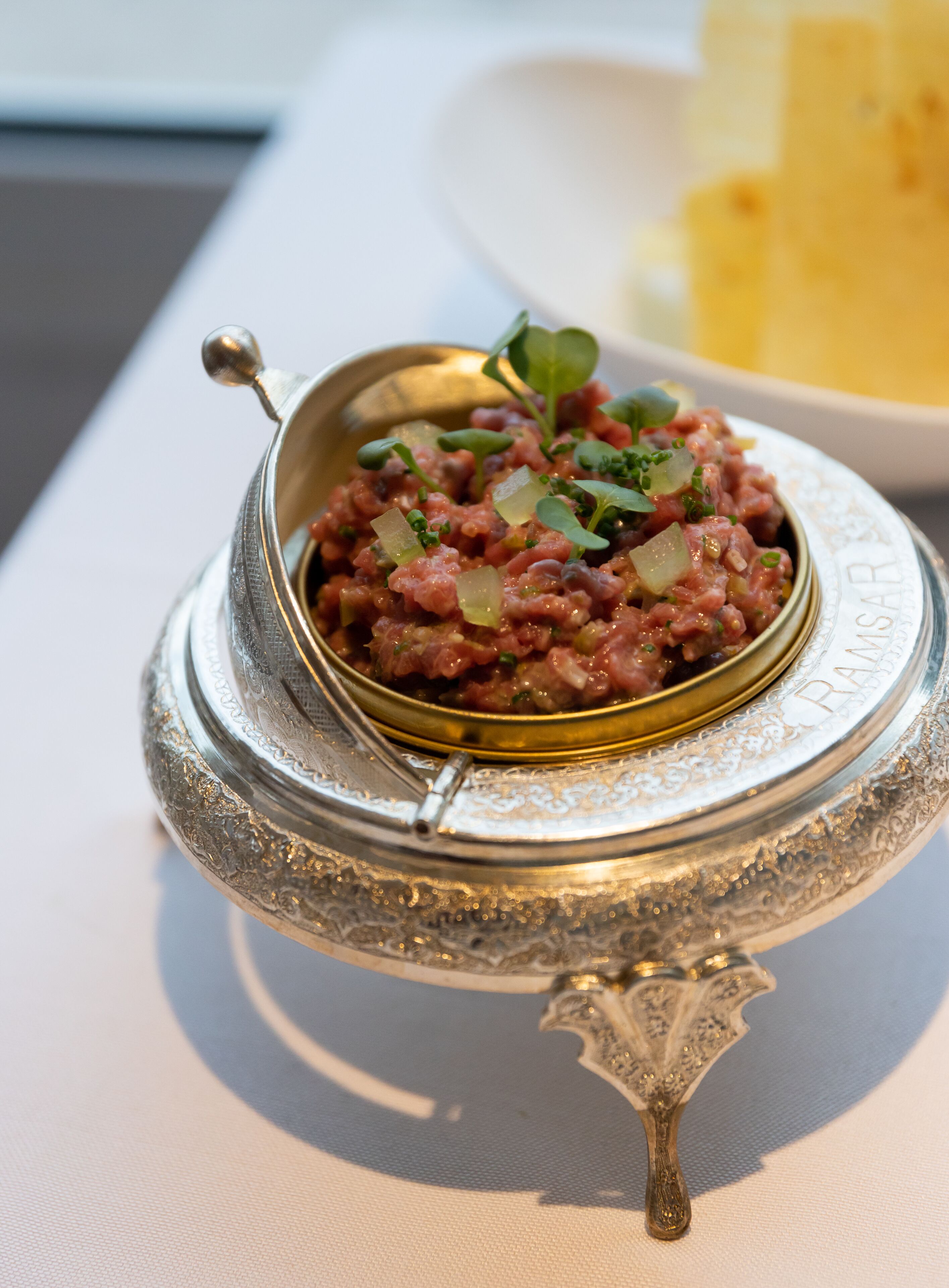 A dish of food in a decorative silver bowl with a handle, placed on a table.