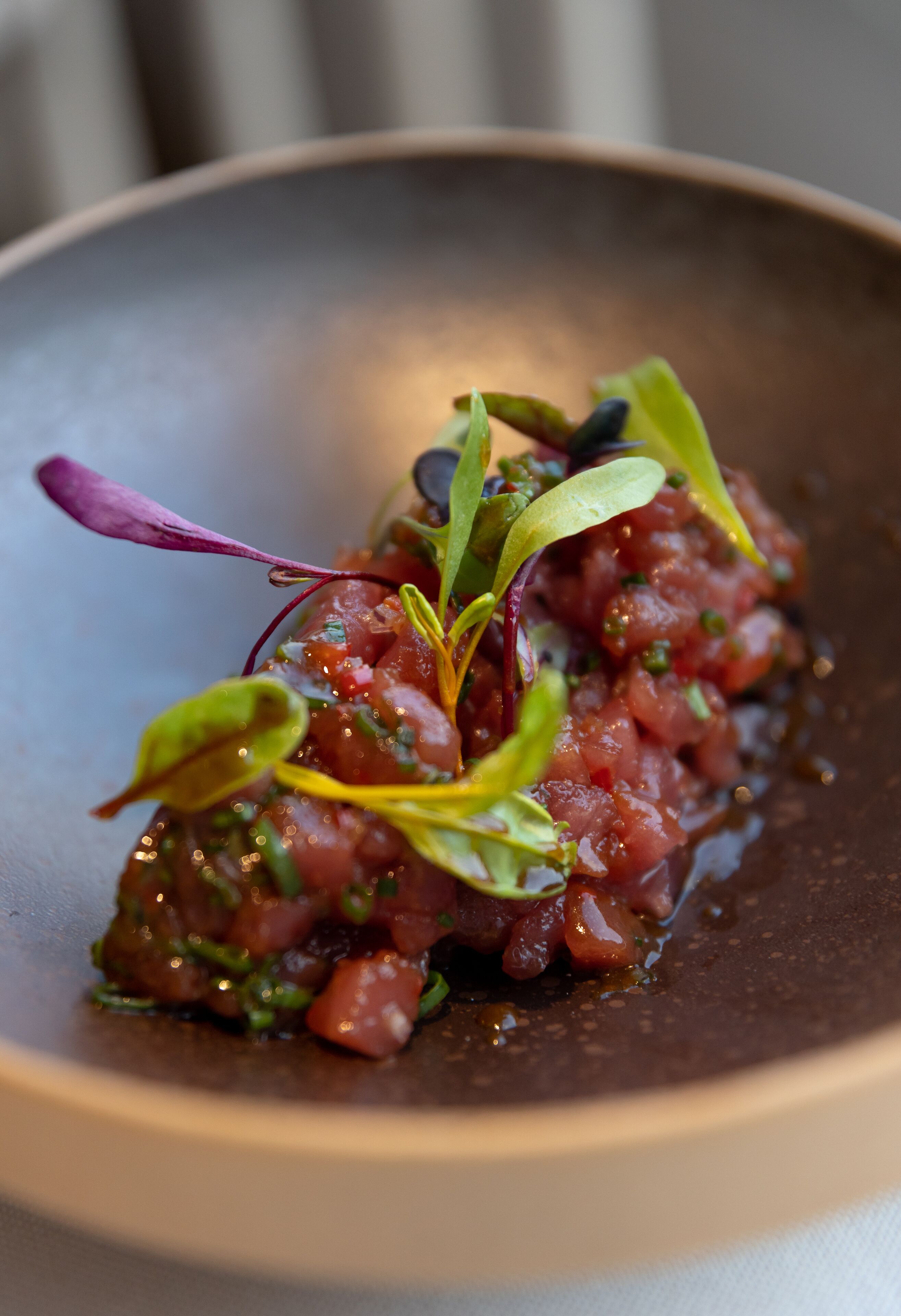 A dish with a dark plate, garnished with green leaves and a purple flower.