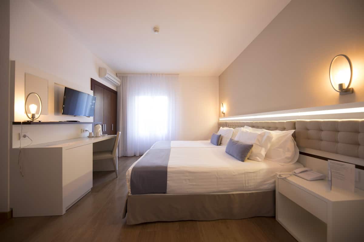 A modern hotel room with a large bed, a desk, a flat-screen TV, and a bedside table with a lamp.
