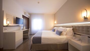 A modern hotel room with a large bed, a desk, a flat-screen TV, and a bedside table with a lamp.