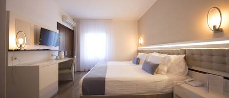 A modern hotel room with a large bed, a desk, a flat-screen TV, and a bedside table with a lamp.