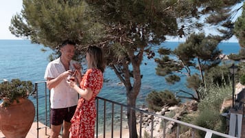 Una pareja está de pie en un balcón con vista al mar y a los árboles.