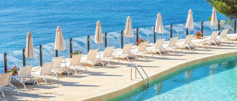 A poolside area with lounge chairs and umbrellas, overlooking a clear blue sea.
