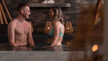 Una pareja en un jacuzzi con un muro de madera y decoración de bambú al fondo.