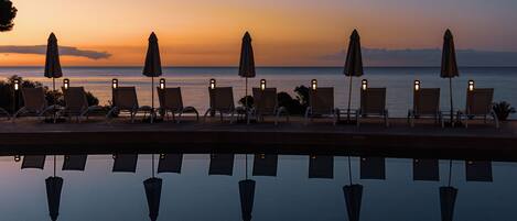 A poolside area with lounge chairs and umbrellas, reflecting the sunset over the water.