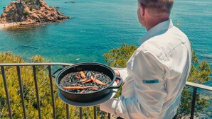 A man holding a pan with grilled seafood on a balcony overlooking a coastal view. - Park Hotel San Jorge & Spa by Escampa Hotels (Calonge)