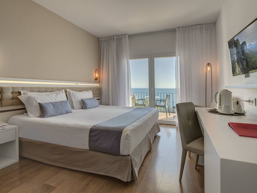 Habitación de hotel con una cama grande, un escritorio, una silla, un televisor y un balcón con vista al mar.