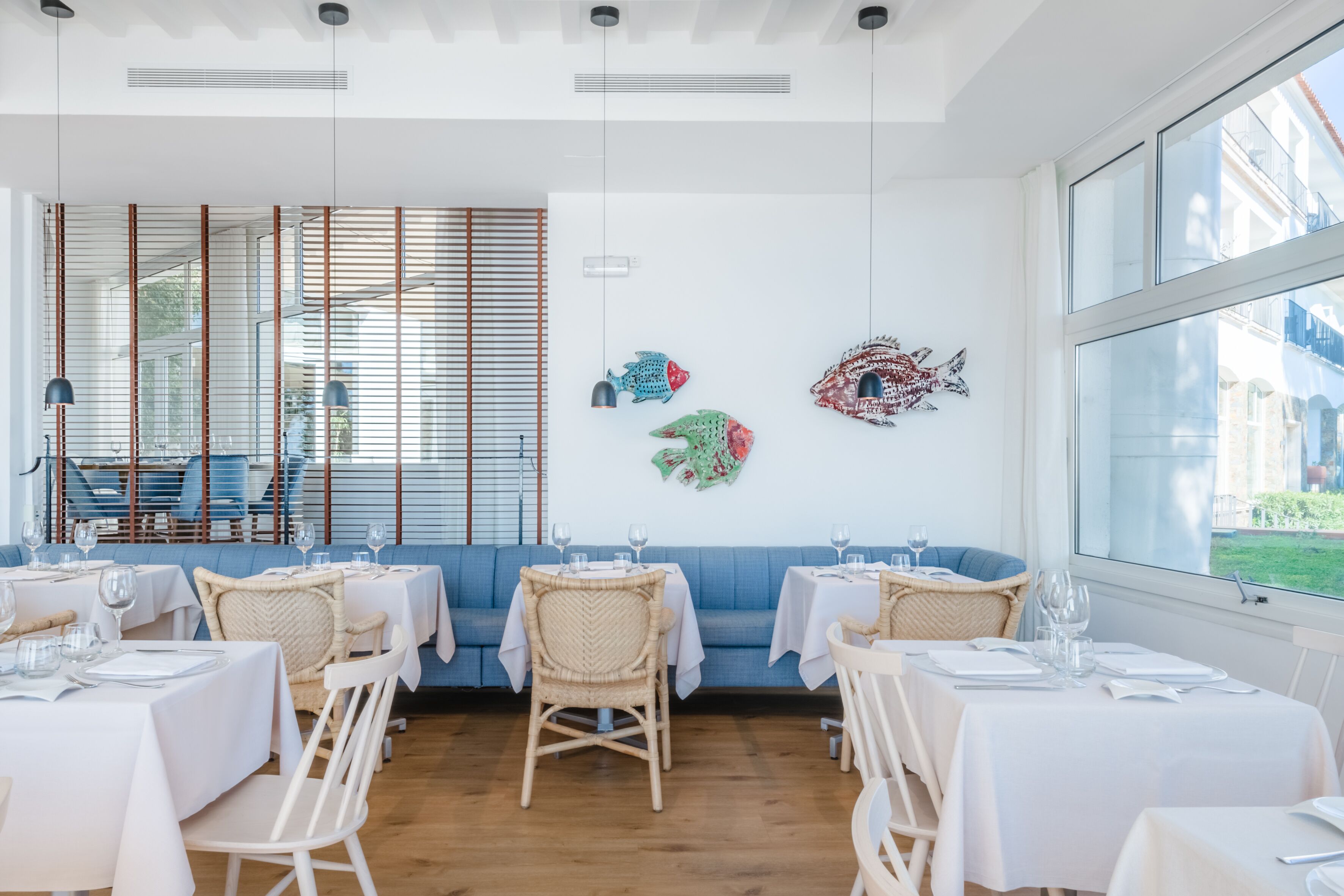 A restaurant with white tables, wicker chairs, and a blue sofa.