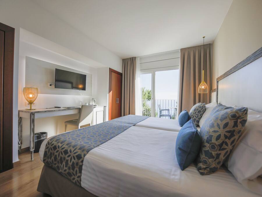 A hotel room with two beds, a desk, a television, and a balcony with a chair.