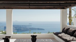 A modern living room with a large window overlooking a scenic coastal view. - Katikies Chromata Santorini - The Leading Hotels of the World (Santorini)