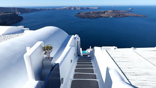 A white-washed building with a staircase leading to a balcony overlooking a blue sea and rocky islands. - Katikies Chromata Santorini - The Leading Hotels of the World (Santorini)