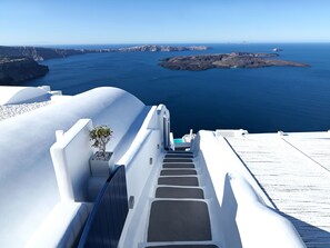 A white-washed building with a staircase leading to a balcony overlooking a blue sea and rocky islands. - Katikies Chromata Santorini - The Leading Hotels of the World (Santorini)