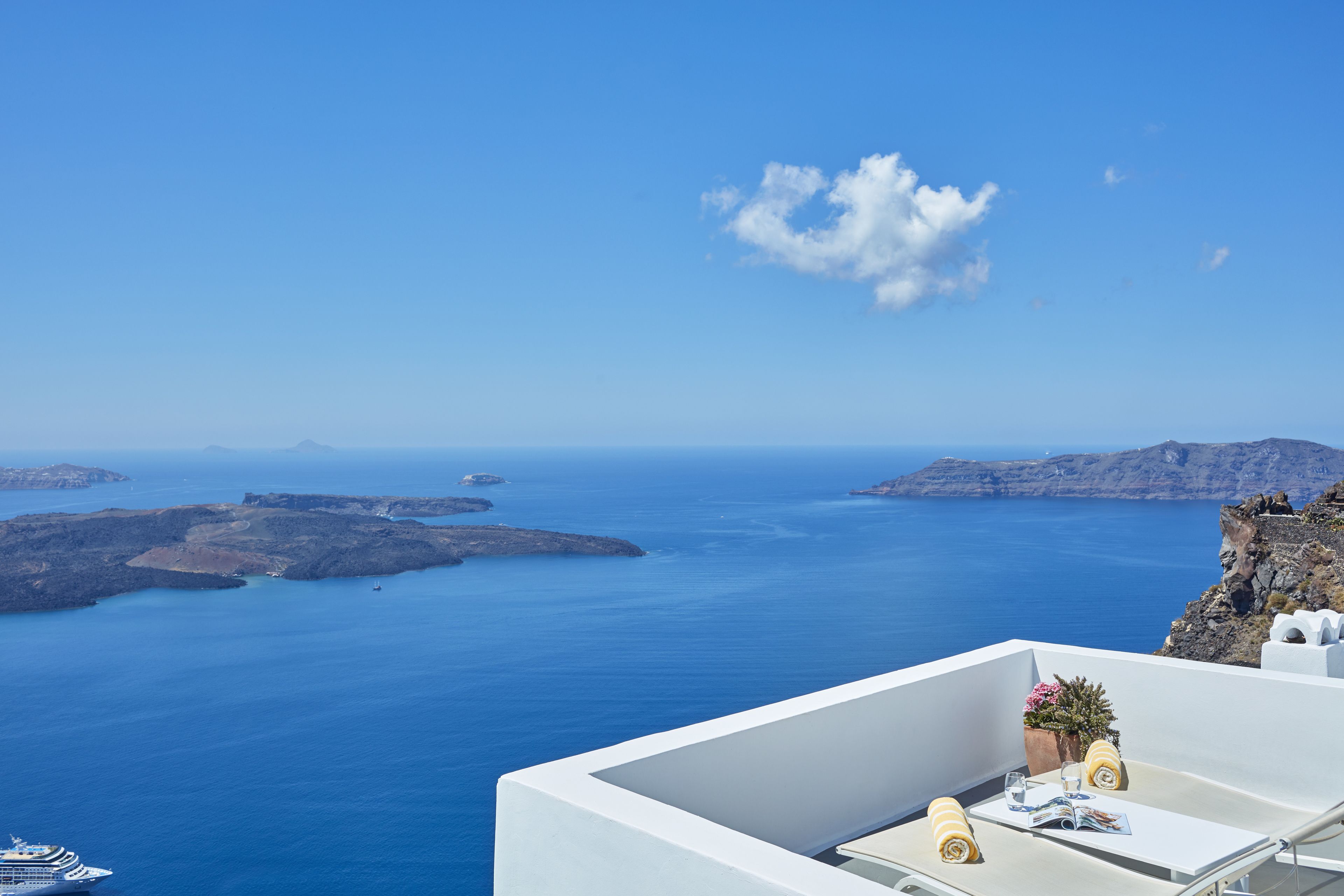 A balcony with a view of the sea, a ship in the distance, and a small table with a plant and a magazine.