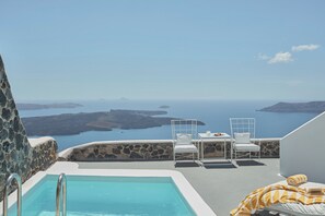 A pool area with a view of the sea and islands, white furniture, and a stone wall. - Katikies Chromata Santorini - The Leading Hotels of the World (Santorini)