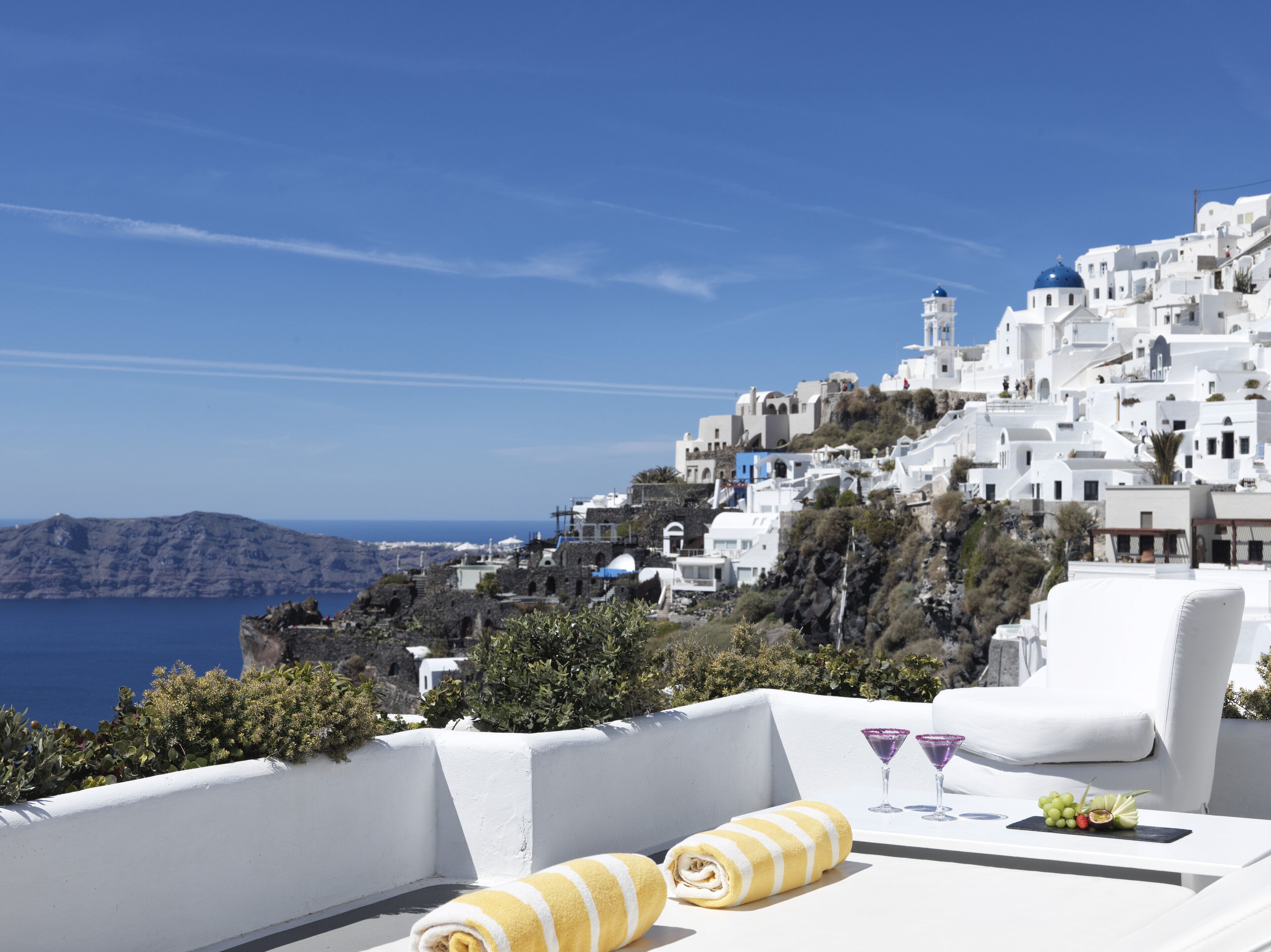 A white-walled building with a view of the sea and a mountain in the background.