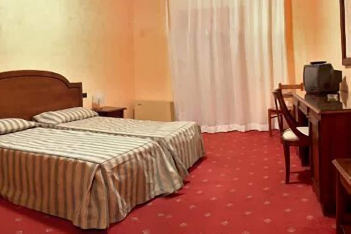 A hotel room with two beds, a desk, a chair, and a television.