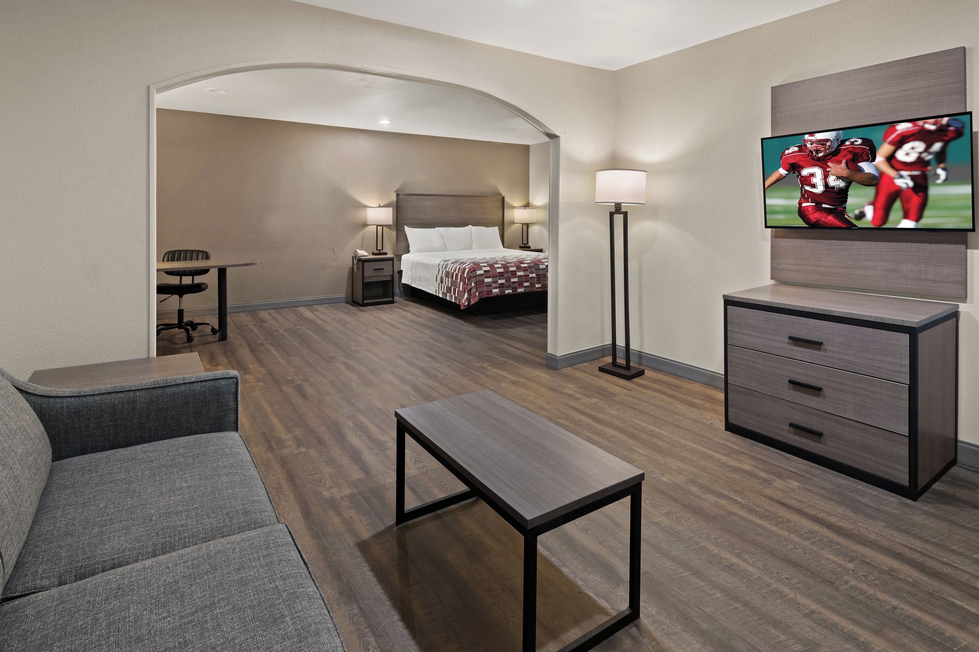 A hotel room with a sofa, a small table, a TV, a bed, and a desk with a lamp.