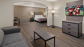 A hotel room with a sofa, a small table, a TV, a bed, and a desk with a lamp.