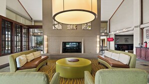 A lobby with a large fireplace, seating area with armchairs and a round table, and a television screen. - Red Roof Inn & Suites Irving – DFW Airport South  (Irving)