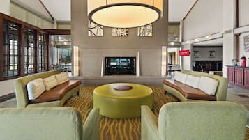 Un hall d’entrée doté d’une grande cheminée, d’un coin salon avec des fauteuils et une table ronde, ainsi que d’un écran de télévision.