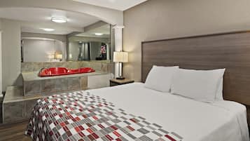 Une chambre d’hôtel avec un grand lit, une baignoire rouge, un meuble-lavabo recouvert de carreaux de marbre, un miroir et un téléviseur.