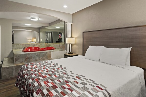 Habitación de hotel con una cama grande, una bañera roja, un tocador con azulejos de mármol, un espejo y un televisor.