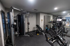 Academia com diversos equipamentos de exercício, incluindo suporte para agachamento, aparelho de supino e máquinas de cardio.