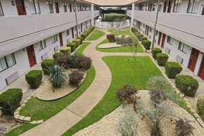 A courtyard with a central pathway, surrounded by neatly trimmed hedges and small trees.