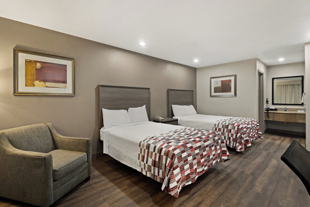 A hotel room with two beds, a chair, a desk, and a mirror.