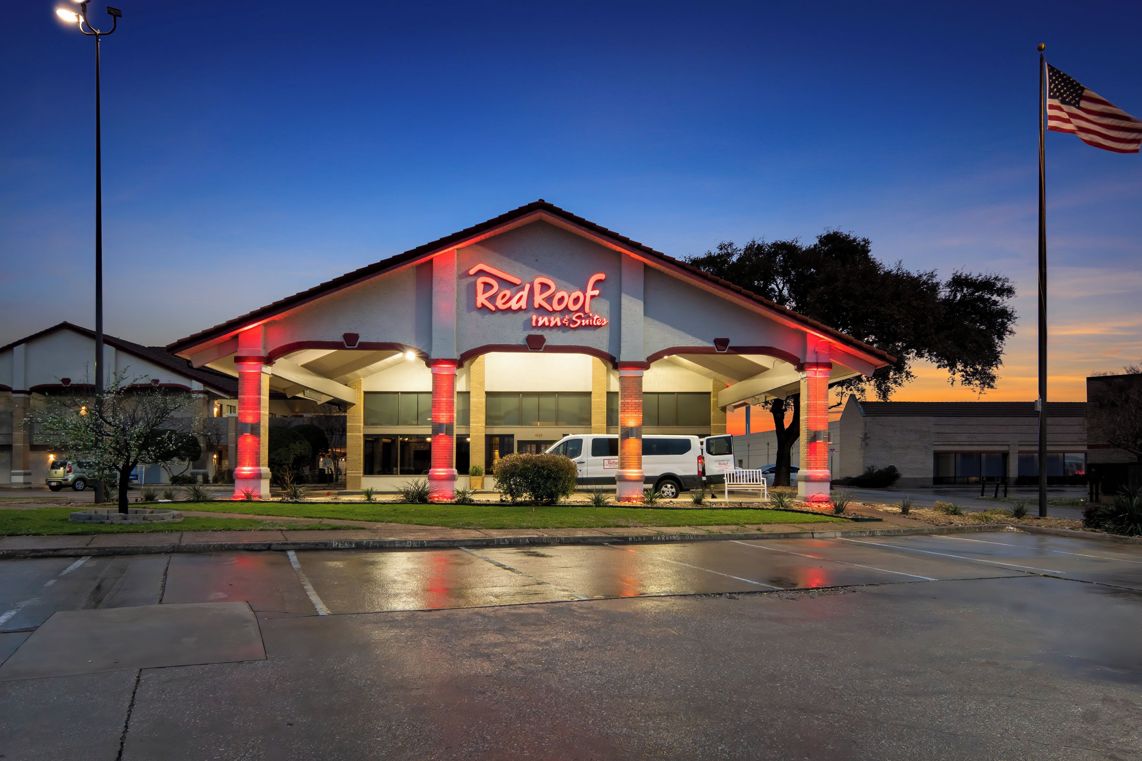 A Red Roof Inn & Suites with a prominent American flag, a parking lot, and a well-lit entrance.