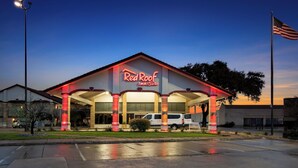 A Red Roof Inn & Suites with a prominent American flag, a parking lot, and a well-lit entrance. - Red Roof Inn & Suites Irving – DFW Airport South  (Irving)