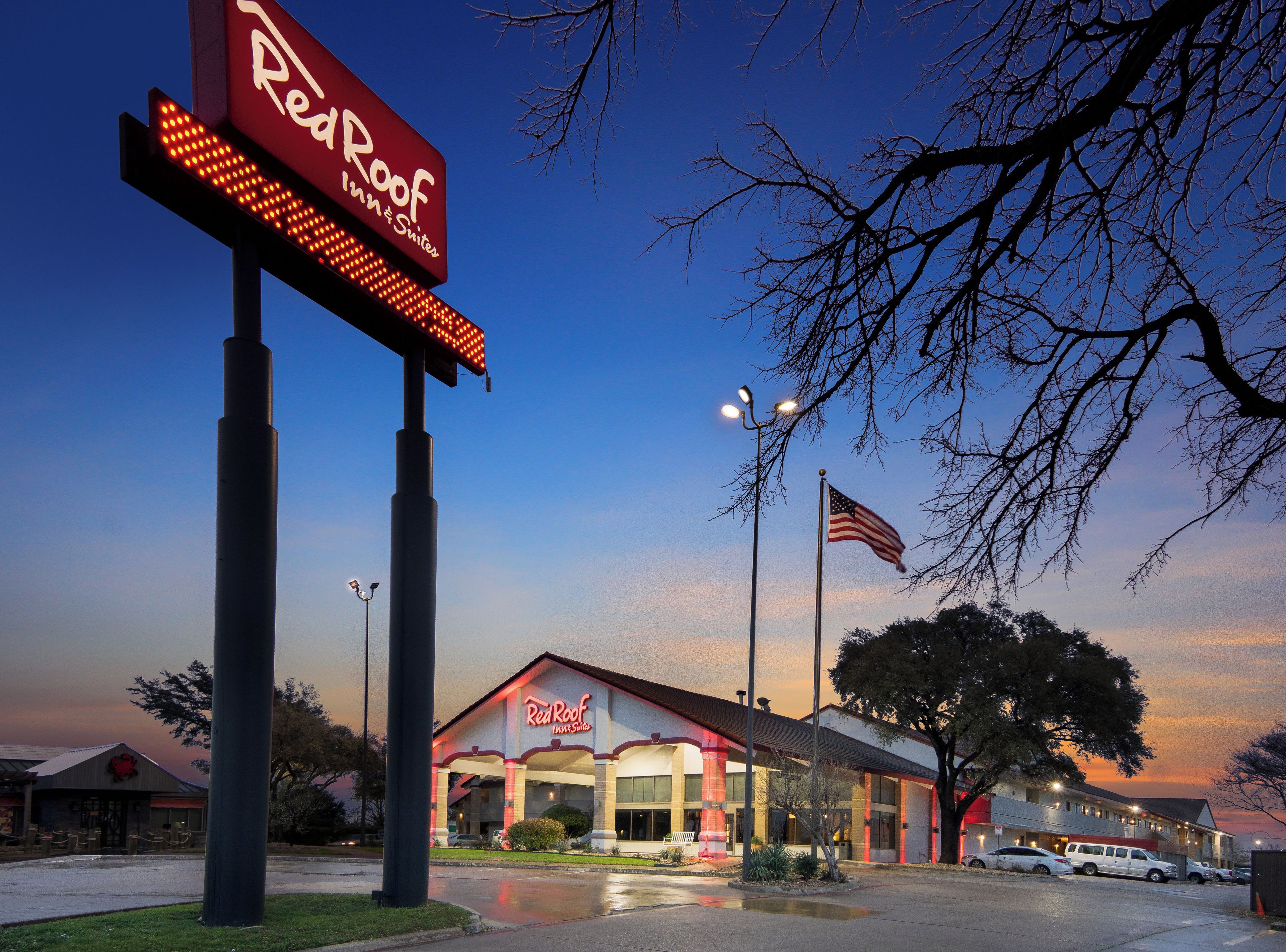 A Red Roof Inn & Suites with a large illuminated sign, an American flag, and a parking lot.