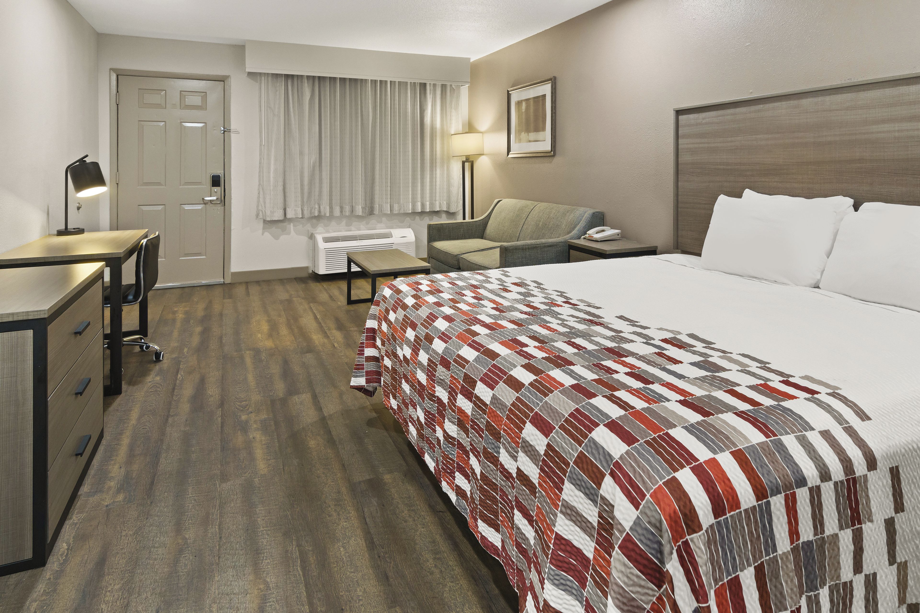 A hotel room with a bed, desk, chair, and a window with curtains.