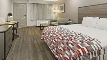 A hotel room with a bed, desk, chair, and a window with curtains.