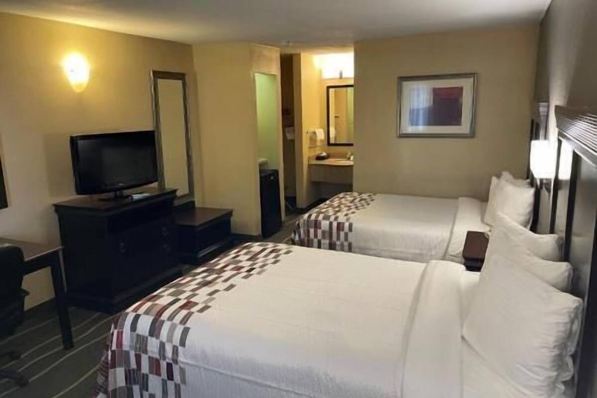 A hotel room with two beds, a TV, a dresser, and a bathroom visible through an open door.