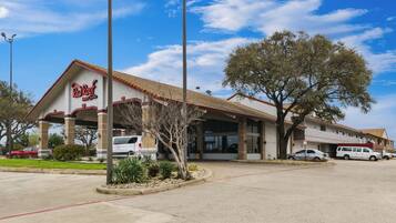 A Red Roof Inn & Suites with a tiled roof, parking area, and a large tree in front.