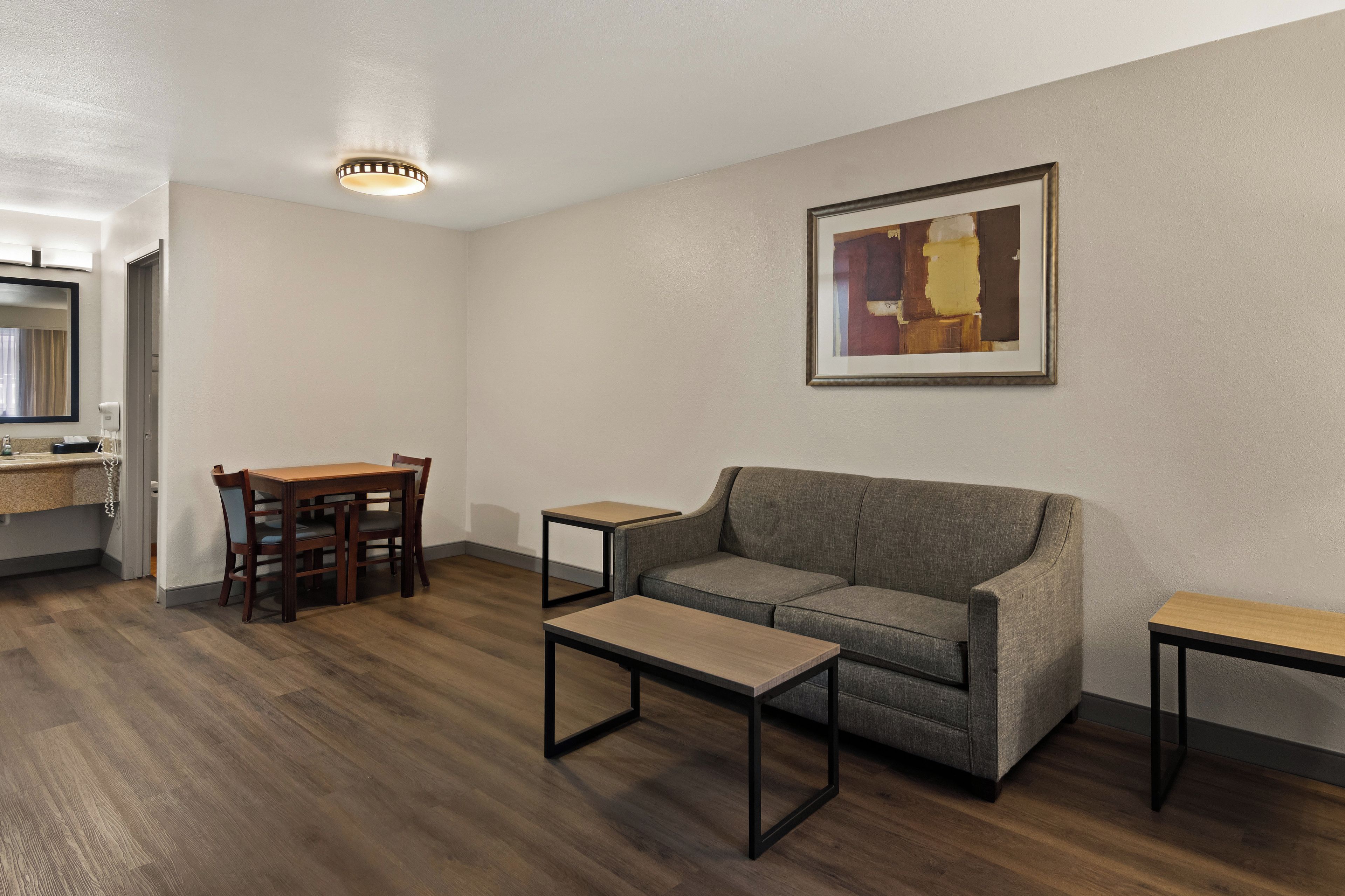 Uma sala de estar moderna com um sofá, uma mesa de centro, uma mesa de jantar com cadeiras, uma pequena mesinha lateral e uma pintura abstrata emoldurada na parede.