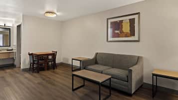 A modern living room with a sofa, a coffee table, a dining table with chairs, a small side table, and a framed abstract painting on the wall.