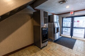 A commercial kitchen with stainless steel appliances, a water dispenser, and a view through the door. - Red Roof Inn & Suites Irving – DFW Airport South  (Irving)