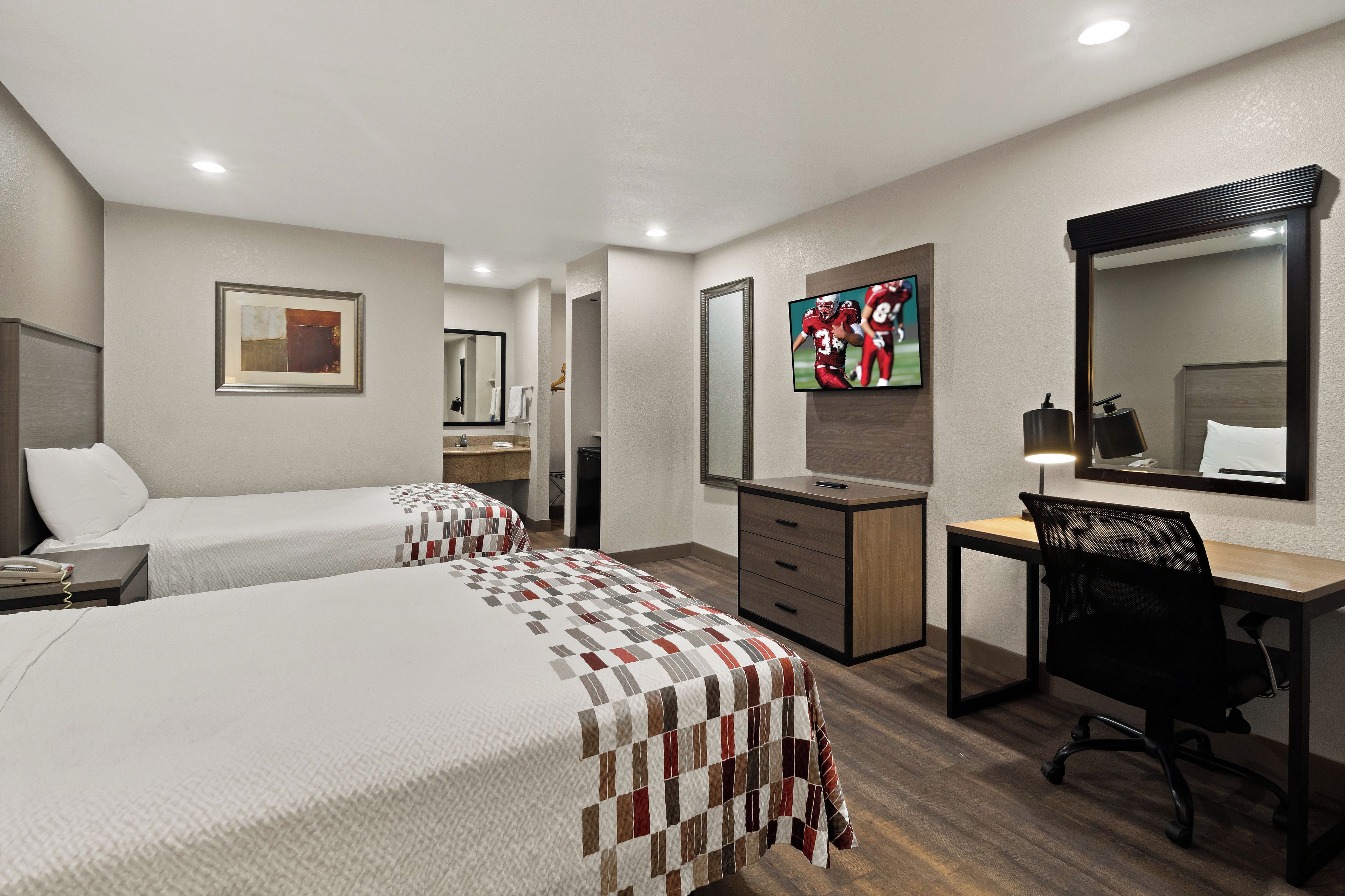 A hotel room with two beds, a desk, a chair, a TV, and a bathroom.