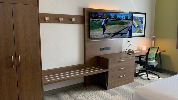 Habitación de hotel con una televisión de pantalla plana grande montada en la pared, un escritorio de madera con una silla, un banco y una cama.