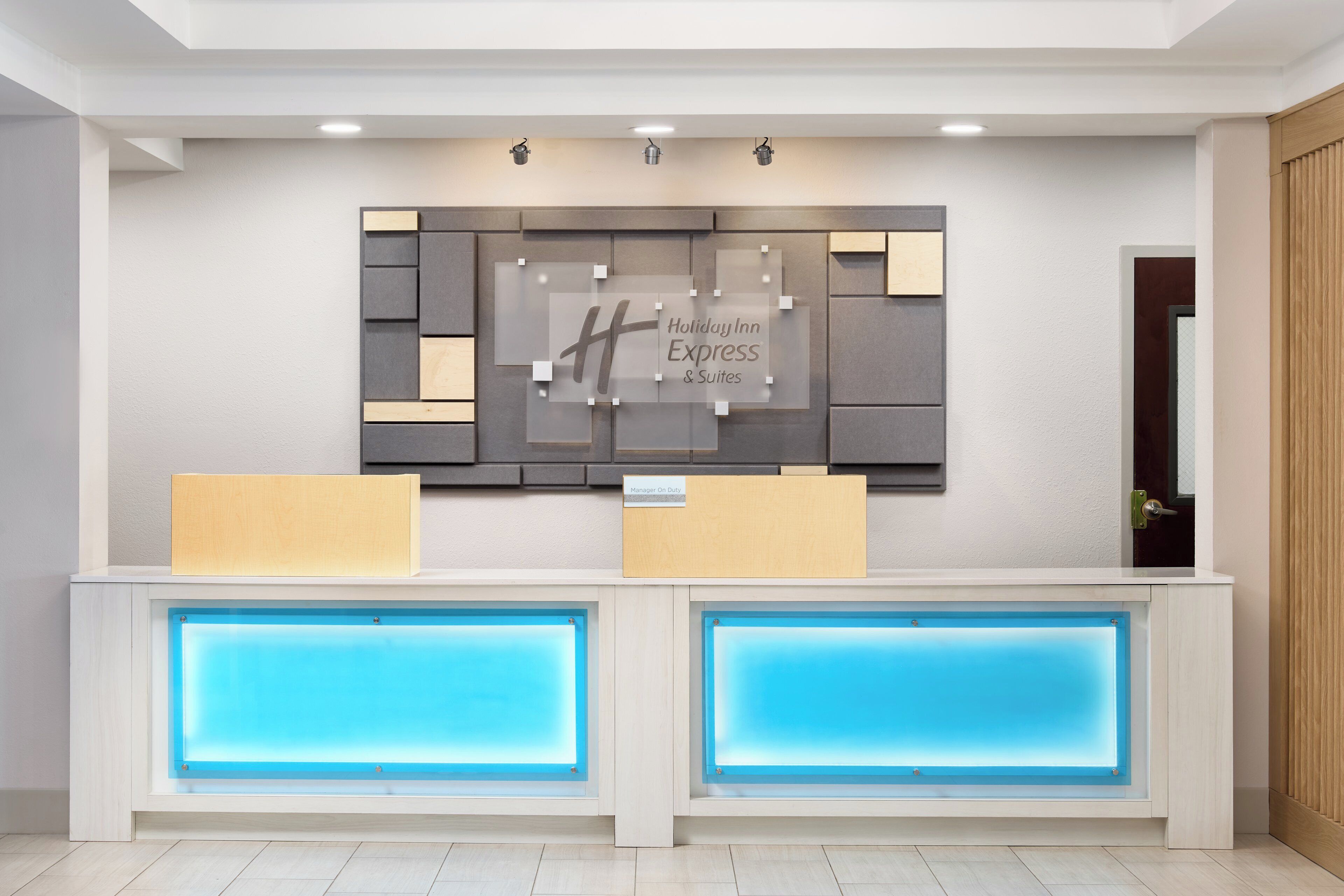 Een modern ontworpen receptiebalie met een groot wandbord en twee verlichte blauwe panelen eronder.