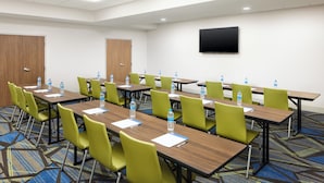 A conference room with multiple tables and chairs, water bottles on each table, and a flat-screen TV mounted on the wall.