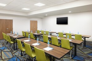 A conference room with multiple tables and chairs, water bottles on each table, and a flat-screen TV mounted on the wall.