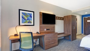 Una habitación de hotel con un escritorio de madera, una silla, un televisor de pantalla plana, un armario y una cama.