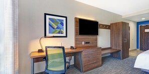 Una habitación de hotel con un escritorio de madera, una silla, un televisor de pantalla plana, un armario y una cama.