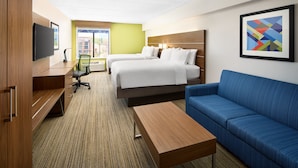 Habitación de hotel con dos camas, un escritorio, un sofá azul, un televisor y una ventana con vistas a edificios.