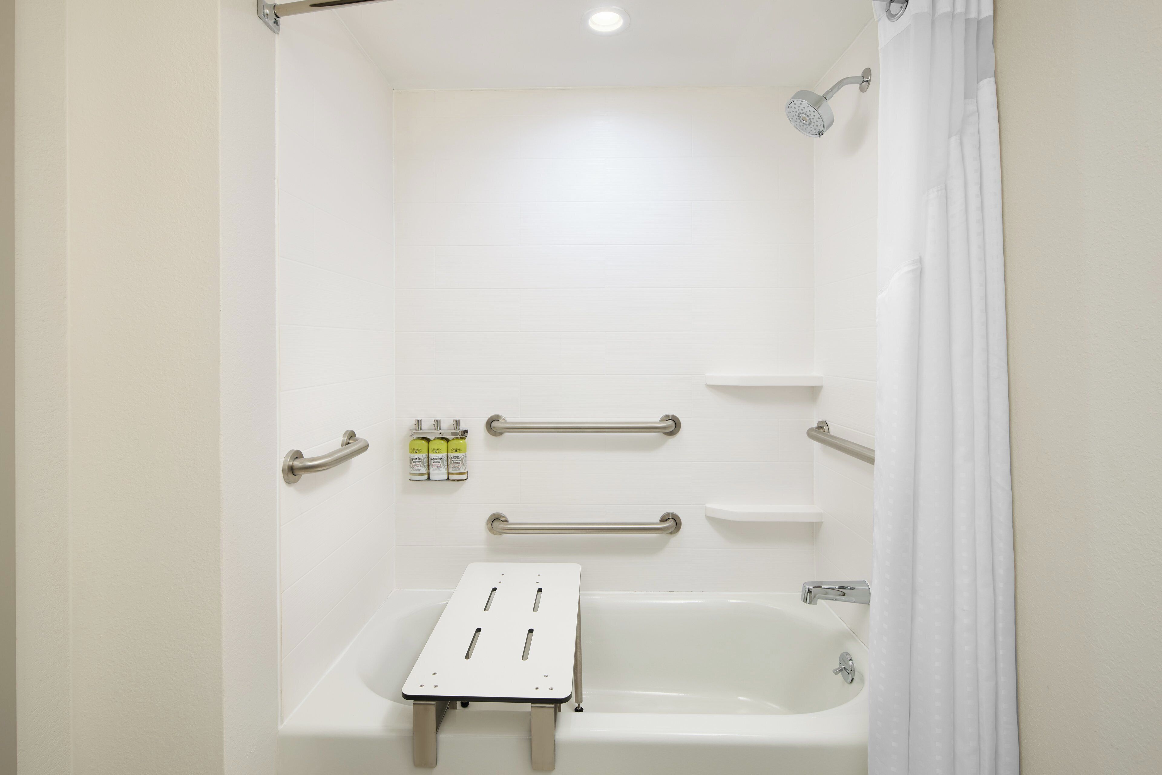 A bathroom with a bathtub, grab bars, and a shelf with toiletries.