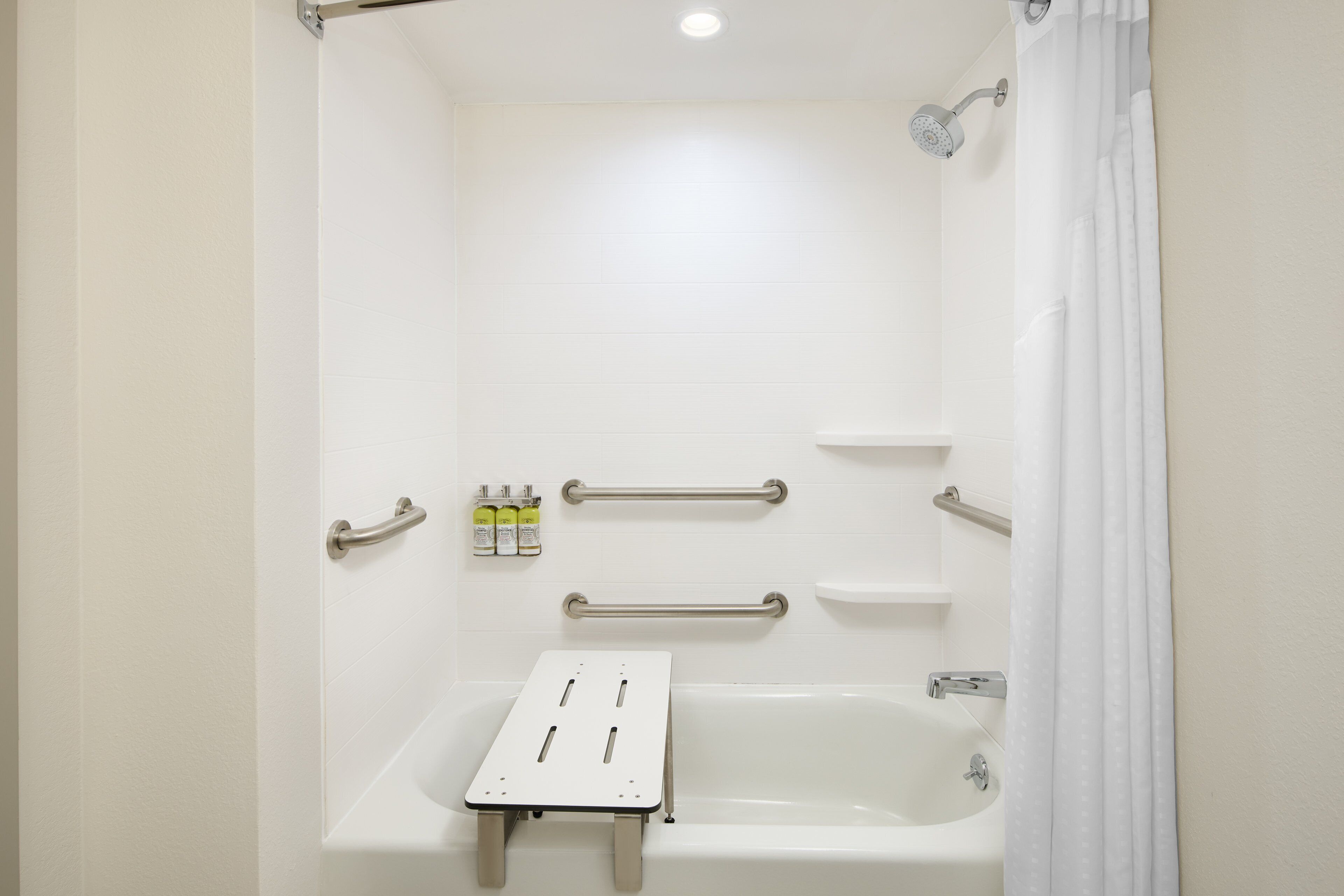 A bathroom with a bathtub, grab bars, a shelf, and a shower curtain.