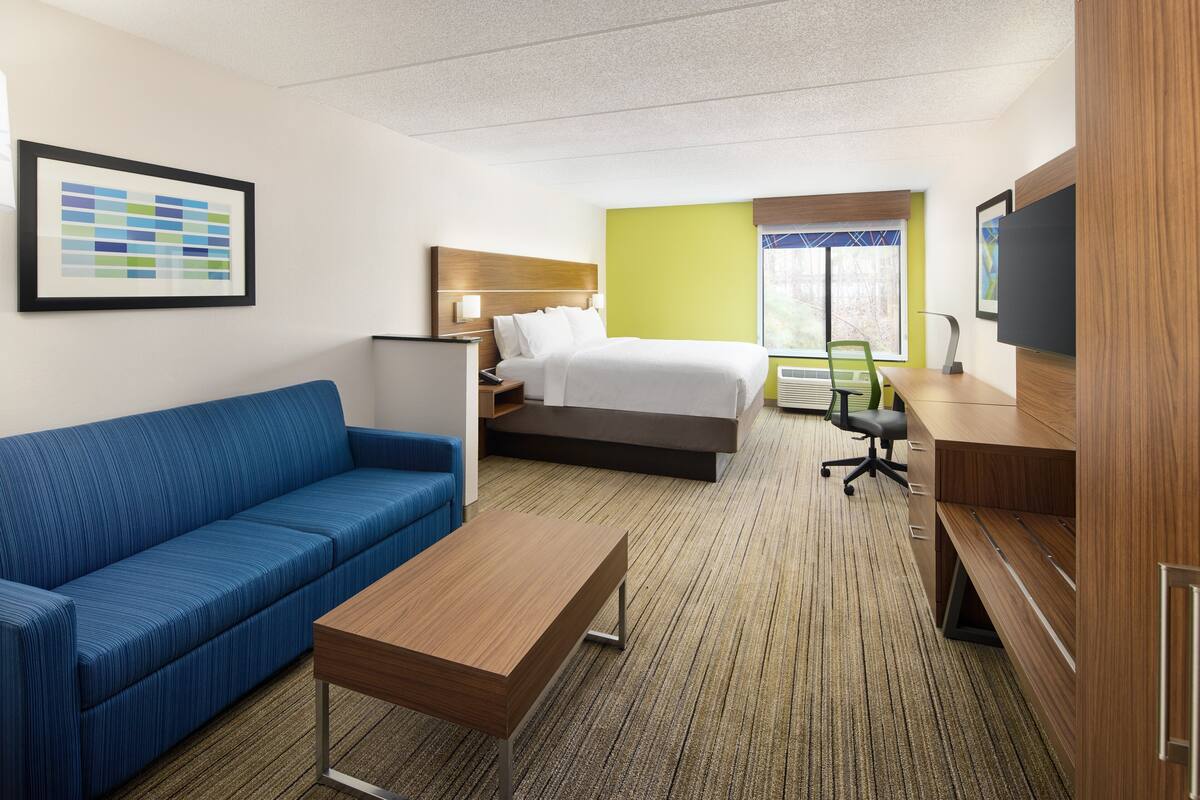 A hotel room with a bed, a blue sofa, a wooden desk, and a television.
